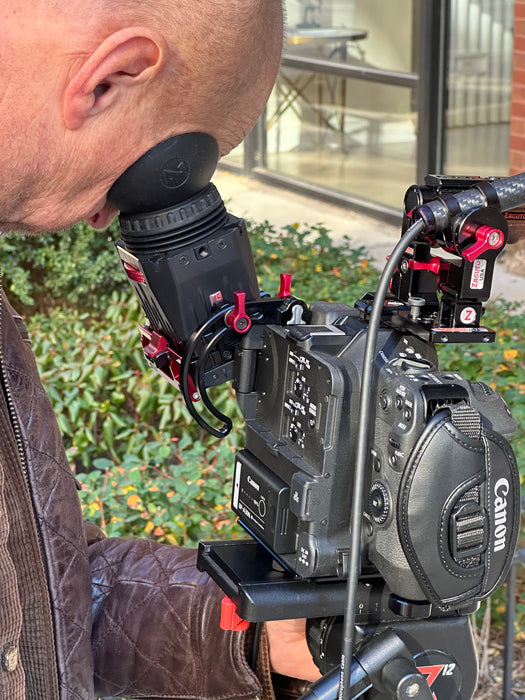 Person holding a Canon video camera outdoors with greenery in the background